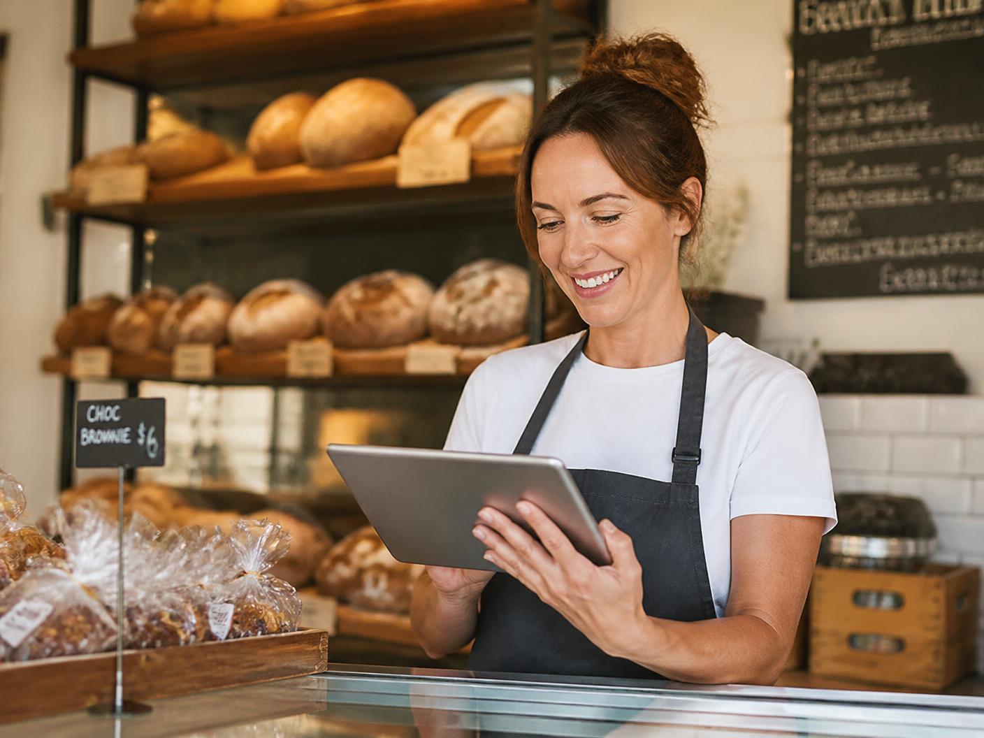 Local bakery owner reviewing her newly designed company website on a tablet behind the shop counter.